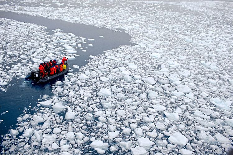 Eine Gruppe Menschen fährt auf einem Boot durch Eiswasser, das Eis ist in kleine Fragmente zerbrochen