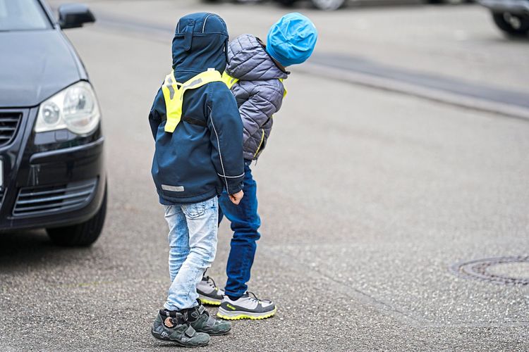 Zwei Kinder überqueren die Straße bei einem parkenden Auto