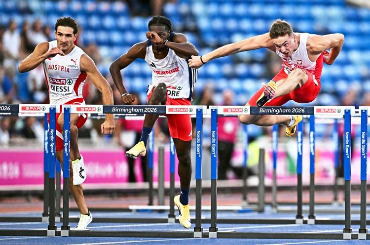Drei männliche Hürdenläufer überwinden nebeneinander eine Hürde während des Halbfinals der 110-Meter-Hürden bei den Leichtathletik-Europameisterschaften 2026 im Alexander-Stadion in Birmingham. Im Hintergrund Zuschauer auf den Tribünen.