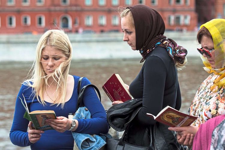 Drei Frauen unterschiedlichen Alters stehen mit Bibeln in der Hand auf einem Platz. 