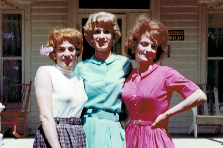 Drei Crossdresser in bunten Kleidern posieren für ein Foto.