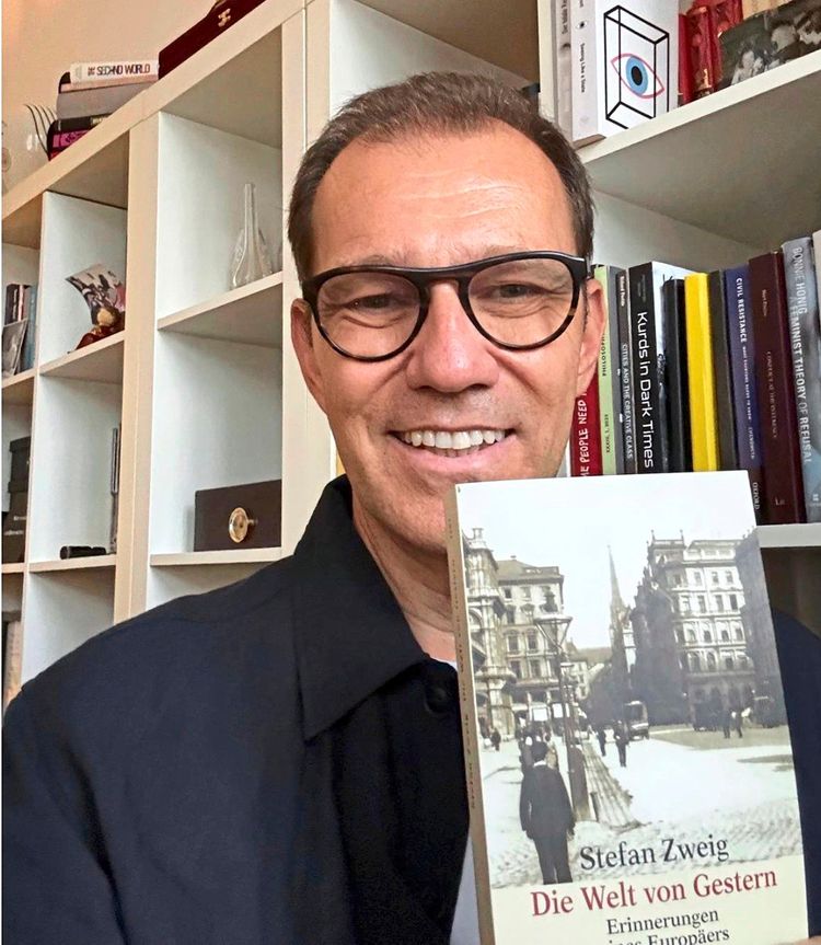 Ein Mann mit Brille hält das Buch „Die Welt von Gestern“ von Stefan Zweig in die Kamera. Im Hintergrund ist ein Bücherregal zu sehen.