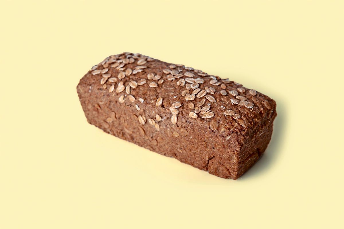 Ein Laib dunkles Roggenbrot, bestreut mit Haferflocken, auf einem hellbeigen Hintergrund.