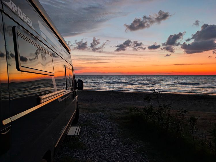 Campervan am Strand vor Meer und Sonnenuntergang
