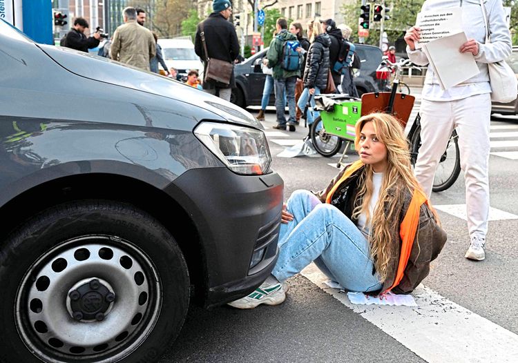Eine Aktivistin hat sich auf Straße geklebt, ein schwarzes Auto stößt an ihre Knöchel