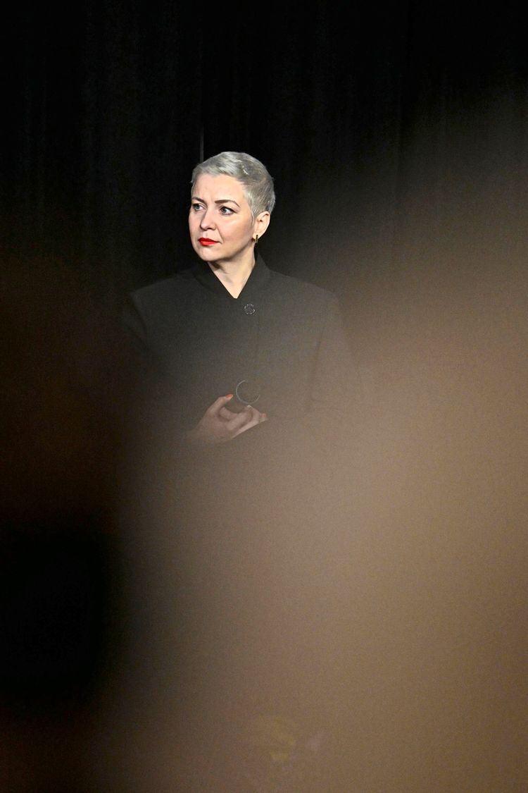 Die belarussische Musikerin und Bürgerrechtlerin Maria Kalesnikava steht in einem dunklen Raum. Sie trägt einen schwarzen Mantel und blickt nachdenklich zur Seite. Ein verschwommener Vordergrund verdeckt teilweise das Bild.