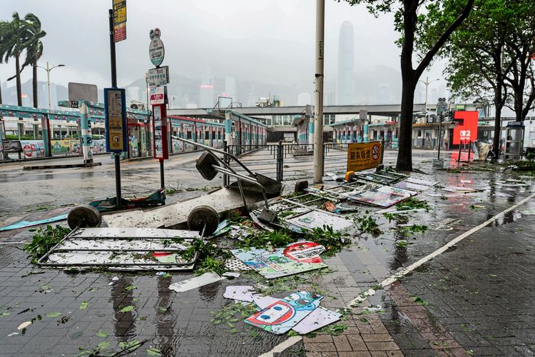 Straßenszene in Hongkong nach dem Durchzug des Taifuns Noul. Auf dem nassen Boden liegen umgestürzte Schilder, Plakate und Zweige. Im Hintergrund sind Gebäude und eine neblige Skyline zu erkennen.