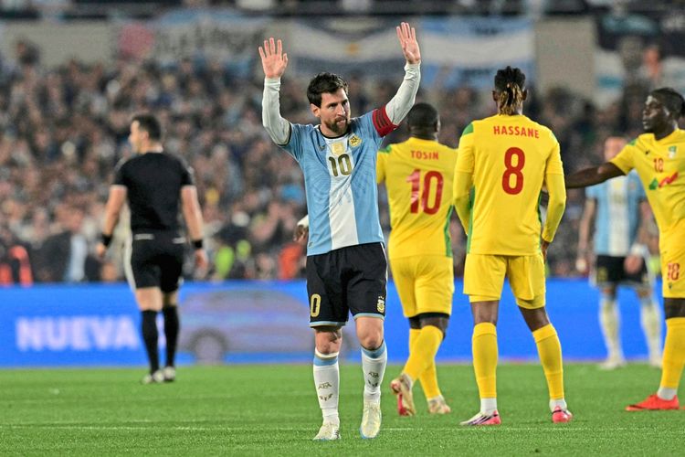 Ein Fußballspieler im Trikot von Argentinien mit der Nummer 10 hebt die Arme, um das Publikum zu grüßen. Im Hintergrund sind andere Spieler zu sehen, darunter Spieler im gelben Trikot von Benin, sowie der Schiedsrichter. Das Bild zeigt eine Szene aus einem Freundschaftsspiel im Mas Monumental-Stadion in Buenos Aires.
