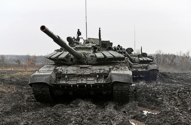 Zwei russische T-72-Panzer auf matschigem Gelände während einer militärischen Übung. Im Hintergrund sind karge Landschaft und Bäume bei grauem Himmel zu sehen.