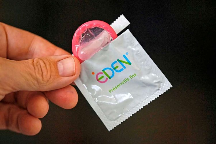 Eine Hand hält eine offene Kondomverpackung, aus der ein rosa Präservativ heraussieht.