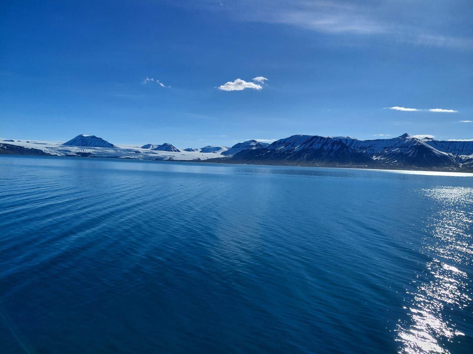 Viel Wasser, im Hitergrund Land mit Fels und Eis unter blauem Himmel
