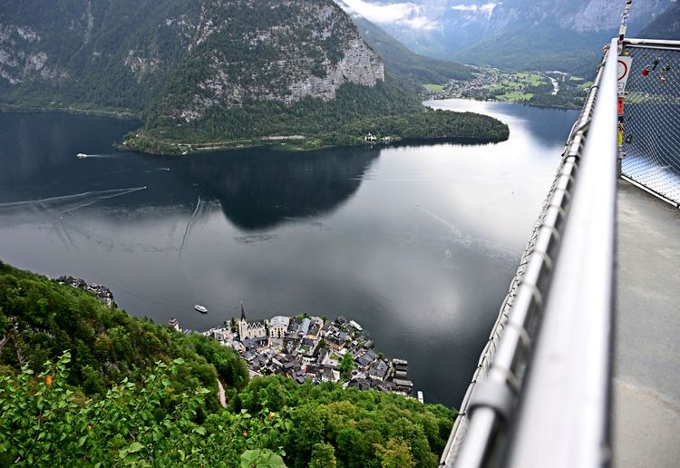 Blick von einer Plattform auf den Ort Hallstatt und den Hallstätter See, umgeben von Wald und Bergen, mit Booten auf dem Wasser.