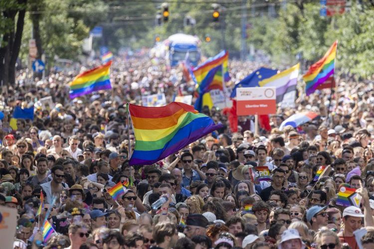 Foto von einer Pride-Parade mit einer Menschenmenge und Regenbogenfahnen.