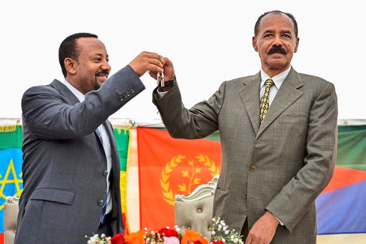 Zwei Männer stehen lächelnd nebeneinander, einer überreicht dem anderen einen Schlüssel. Im Hintergrund sind die Flaggen von Äthiopien und Eritrea zu sehen.