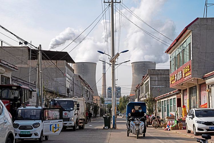Ein Kohlekraftwerk, ist in Betrieb, während Menschen eine Straße in Dingzhou, Baoding, in der nordchinesischen Provinz Hebei entlanggehen.