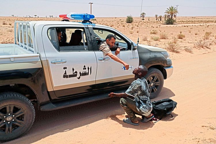 Ein libyscher Grenzbeamter gibt einem Migranten Wasser aus dem Auto