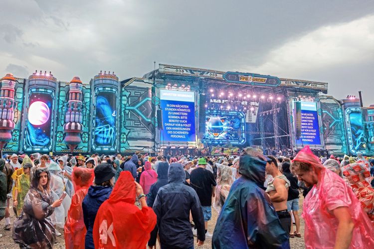 Eine Menschenmenge in Regenponchos vor der mit futuristischen Bildschirmen gestalteten 