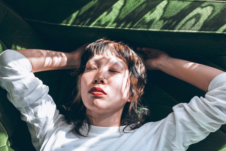 Junge asiatisch-gelesene Frau liegt mit geschlossenen Augen auf dem Sofa