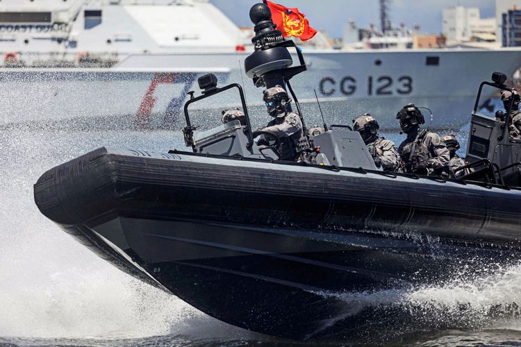 Mitglieder der Spezialeinheit der taiwanesischen Küstenwache (STU) fahren in einem schnellen, schwarzen Schlauchboot mit hoher Geschwindigkeit über das Wasser. Sie tragen taktische Ausrüstung und Helme, während sie an einer maritimen Übung in Kaohsiung am 8. Juni 2025 teilnehmen. Im Hintergrund ist ein großes Schiff mit der Aufschrift „CG 123“ sichtbar. Eine rote Flagge weht am Bootsmast.