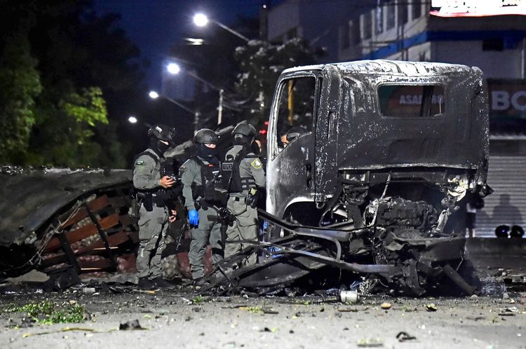 Polizisten inspizieren die Überreste eines durch eine Explosion beschädigten LKWs in Cucuta, Kolumbien, bei Nacht. Teile des LKWs sind schwer beschädigt, während die Umgebung in Dunkelheit beleuchtet ist.