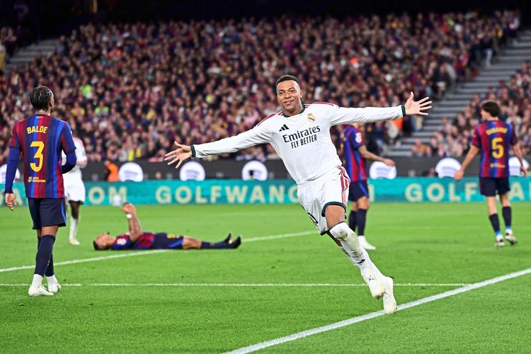 Ein Fußballspieler von Real Madrid, in einem weißen Trikot mit ausgebreiteten Armen, feiert ein Tor auf dem Spielfeld. Im Hintergrund sind Spieler des FC Barcelona in blau-rot gestreiften Trikots und ein vollbesetztes Stadion zu sehen.