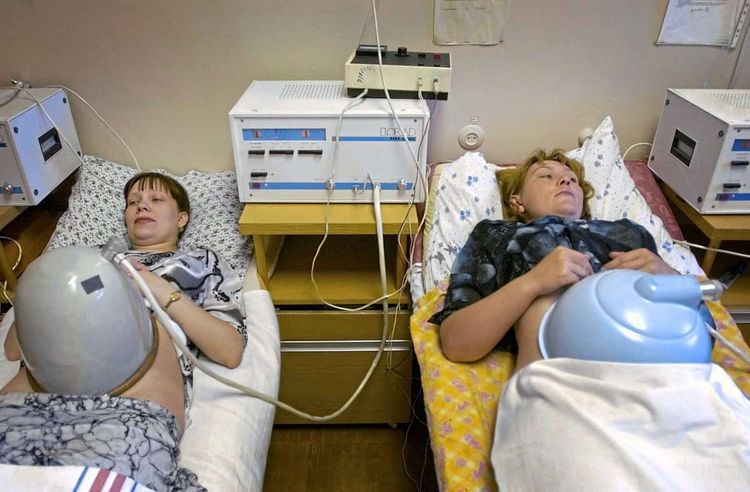 Zwei schwangere Frauen liegen auf Krankenhausbetten, ihre Bäuche sind mit medizinischen Instrumenten bedeckt. 