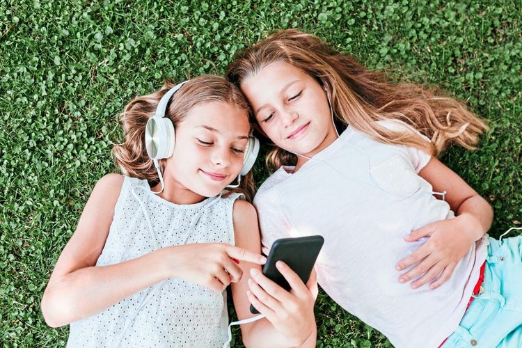 Zwei Mädchen, Freundinnen, sitzen im Gras und hören gemeinsam Musik