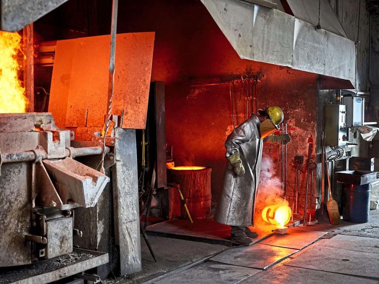 Man steht bei Hochofen und gießt heißes Metall in eine Form.