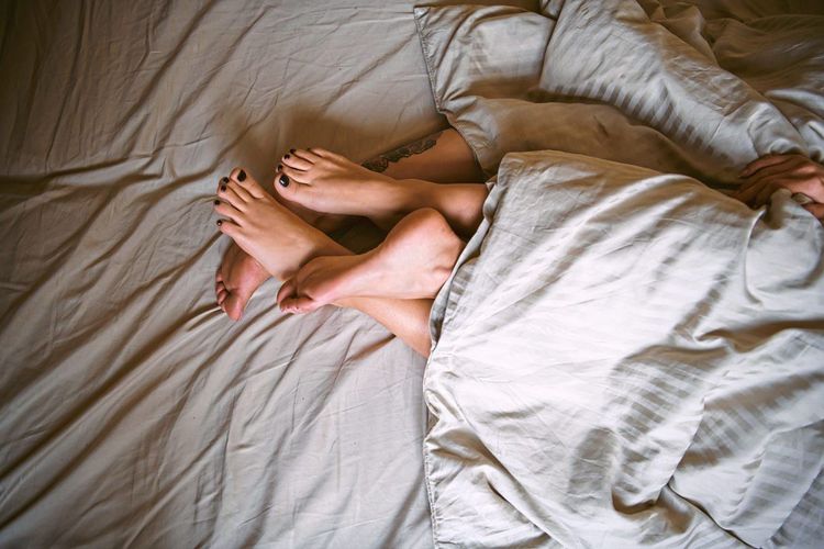 Füße eines Paares ragen aus einer Bettdecke. 