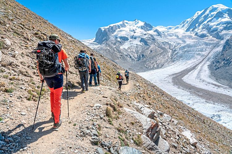 Menschen wandern mit Rucksäcken und Wanderstöcken auf einem Gletscher