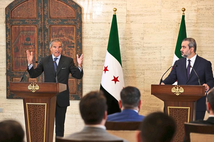Zwei Männer stehen hinter Rednerpulten während einer gemeinsamen Pressekonferenz in einem Innenraum mit syrischen Flaggen im Hintergrund. Der Mann links gestikuliert mit erhobenen Armen, während der Mann rechts ihm zuhört.