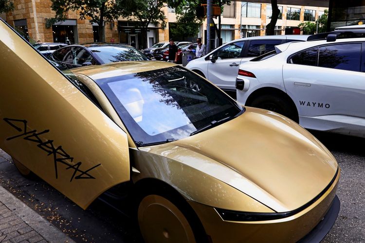 Ein goldfarbener Tesla Cybercab mit geöffneter Tür steht in der Innenstadt von Austin, Texas, neben einem weißen Fahrzeug mit der Aufschrift 