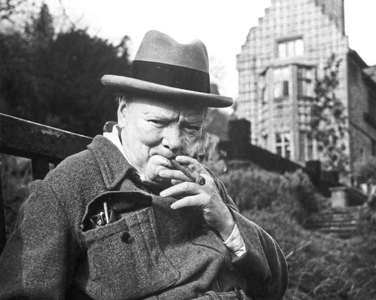Der britische Premier Winston Churchill mit Hut und Zigarre in seinem Garten sitzend