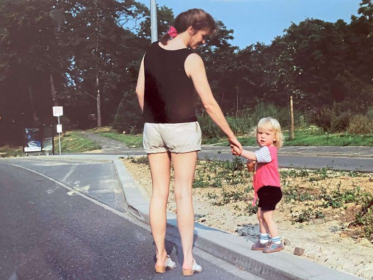 Ein kleines, blondes Mädchen geht mit seiner Mutter an der Hand auf der Straße