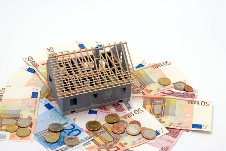 Ein unfertiges Modell eines Einfamilienhauses steht auf Euro-Scheinen und Münzen.