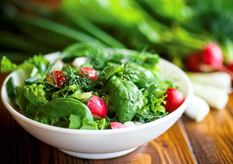 Spring salad from early vegetables, lettuce leaves, radishes and herbs in a white bowl süßer Salat