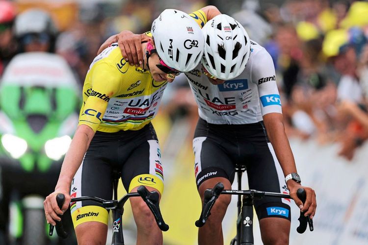 Zwei Radfahrer des Teams UAE Team Emirates fahren nebeneinander über die Ziellinie. Der Fahrer im gelben Trikot des Gesamtführenden legt den Arm um den Fahrer im weißen Trikot des besten Nachwuchsfahrers. Im Hintergrund sind ein Begleitfahrzeug und Zuschauer zu sehen.