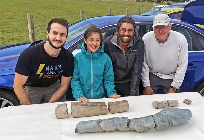 Vier Menschen, darunter ein junges Mädchen, stehen grinsend vor einem Tisch mit Teilen eines fossilen Knochens.