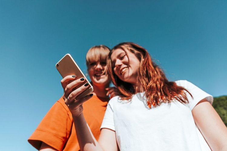 Zwei junge Frauen stehen nebeneinander und schauen auf ein Smartphone