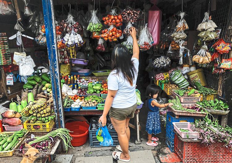 Eine Frau auf den Philippinen steht vor einem Marktgeschäft mit Gemüse und Obst.