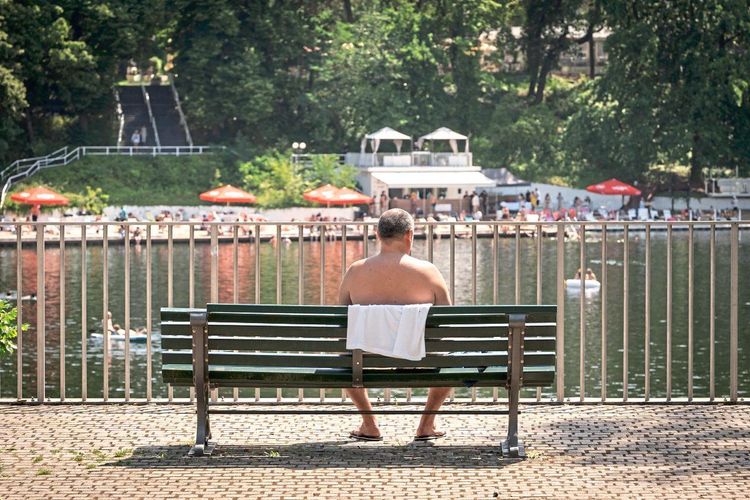 Ein Mann sitzt auf einer Bank und schaut aufs Wasser