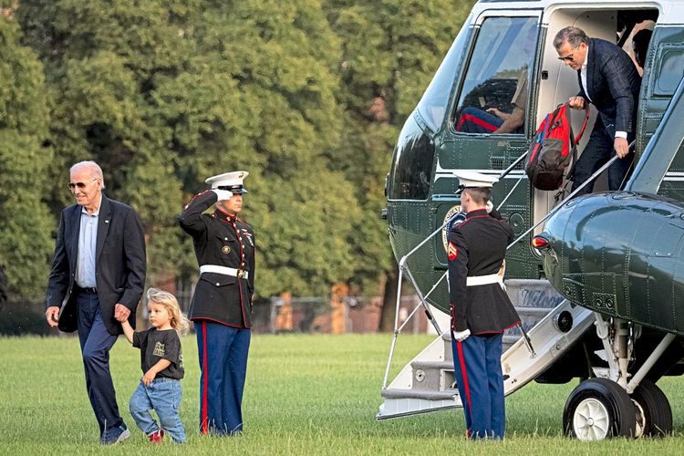 US-Präsident Joe Biden hält seinen Enkelsohn an der Hand, hinter ihnen ein Hubschrauber, aus dem Sohn Hunter steigt.