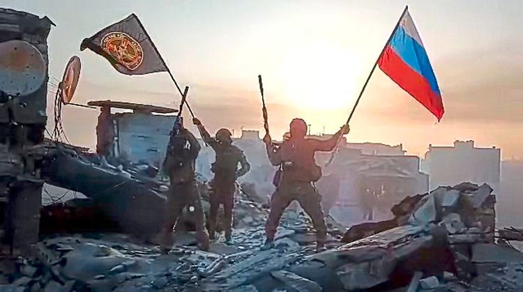 Wagner-Söldner schwenken die russische Flagge und die Flagge der Söldnertruppe über den Ruinen von Bachmut.
