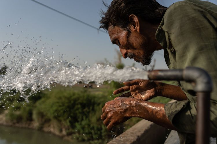 Mann benässt seine Hände mit einem Wasserstrahl, der aus einem Metallrohr kommt