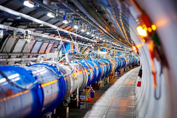 Ein Blick in den Tunnel des Large Hadron Collider (LHC) der Europäischen Organisation für Kernforschung (CERN) zeigt eine Reihe von blauen Dipolmagneten, die verwendet werden, um die Bahn beschleunigter Protonen zu lenken. Die Szene ist hell beleuchtet und zeigt technische Geräte und Kabel entlang der Struktur.