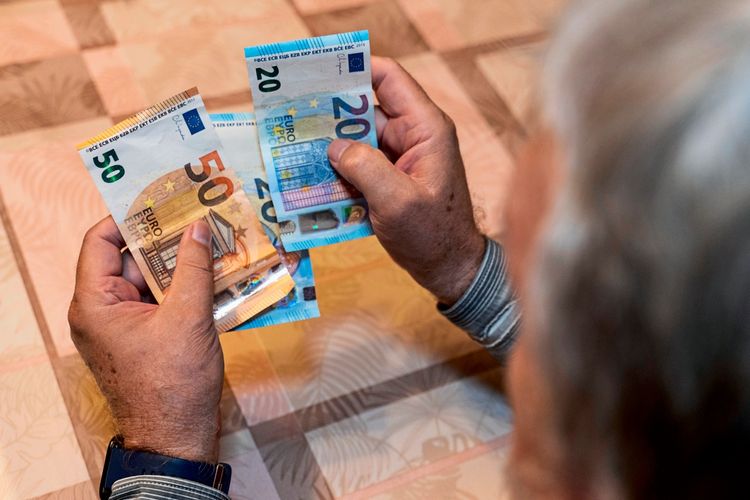 Ein älterer Mann zählt Euroscheine (20- und 50-Euro-Scheine) an einem Tisch.