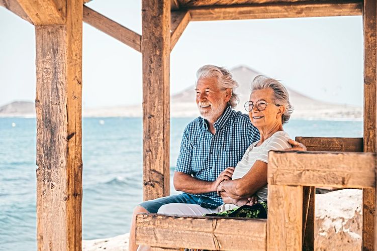 Ein älteres Paar sitzt mit seligem Gesichtsausdruck auf einer Bank mit Blick aufs Meer
