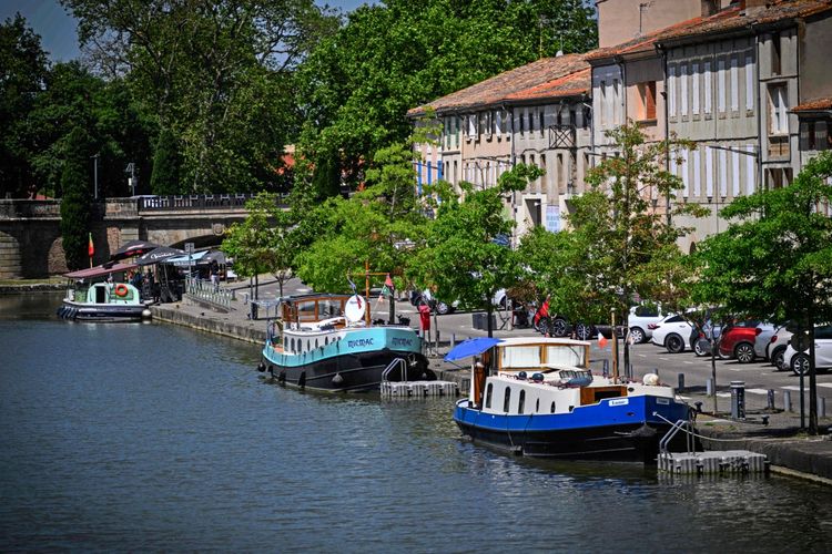 Boote sind am Hafen von Castelnaudary am Canal du Midi in Südwestfrankreich festgemacht, umgeben von Gebäuden, Bäumen und geparkten Autos.