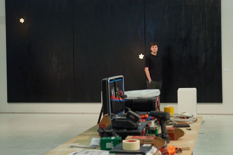 Der Künstler vor einem großen schwarzen Gemälde.