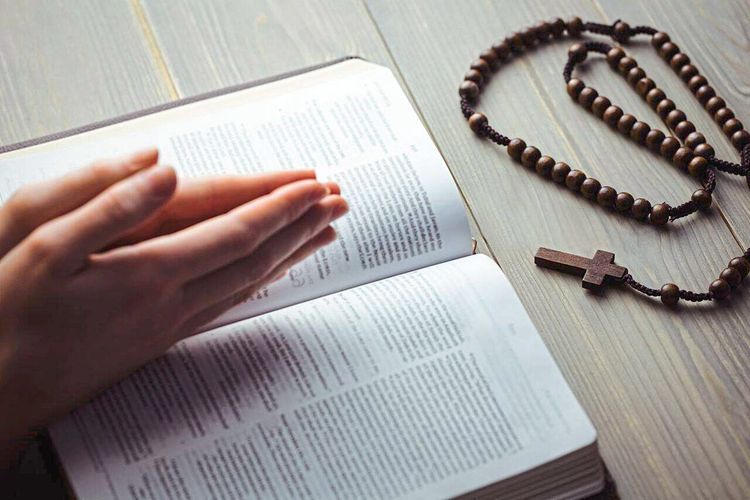 Frau betet mit Bibel und Rosenkranz auf dem Tisch